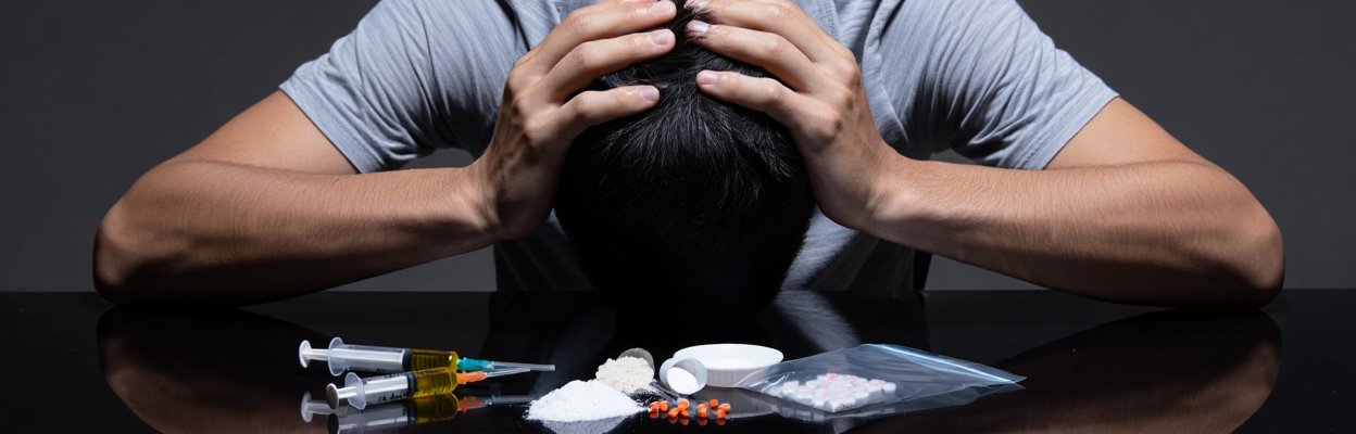 Мужчина с опущенной головой перед столом с веществами